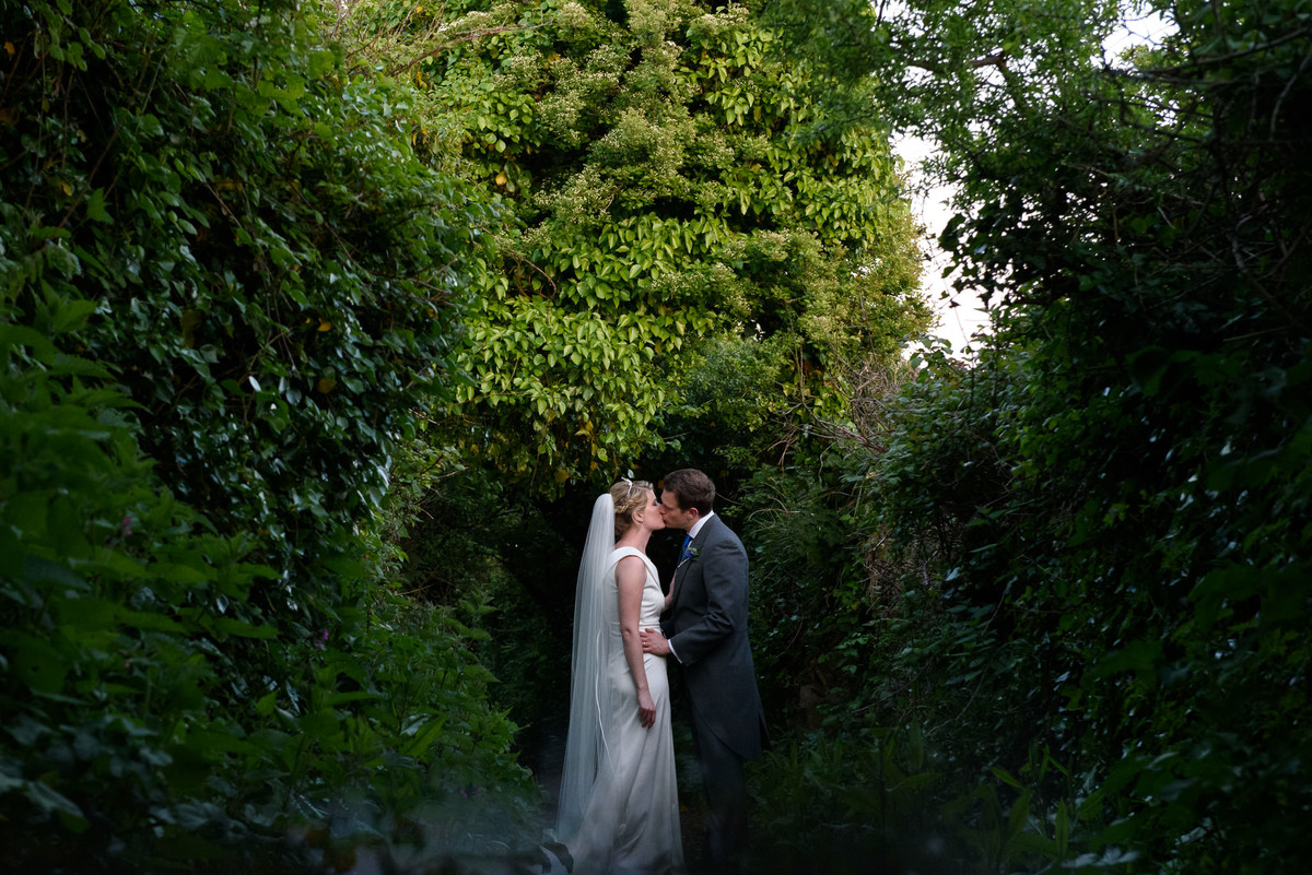 bride and groom kissing in tree tunnel to the coast